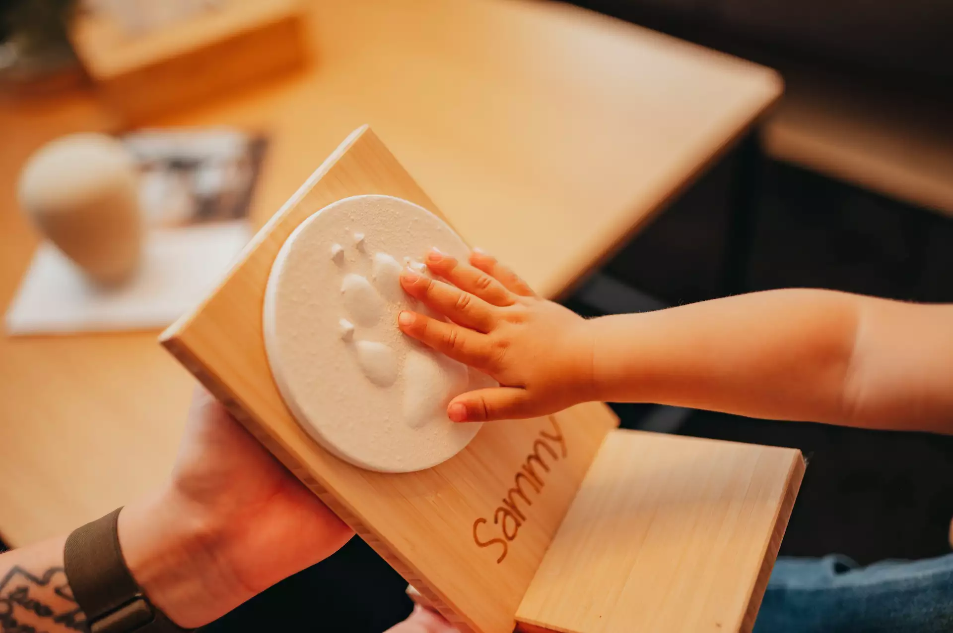 Nahaufnahme einer Kinderhand, die einen weißen, runden Pfotenabdruck auf einer Holzgedenkplatte berührt.